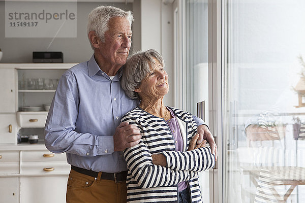 Porträt eines selbstbewussten Seniorenpaares beim Blick durchs Fenster zu Hause