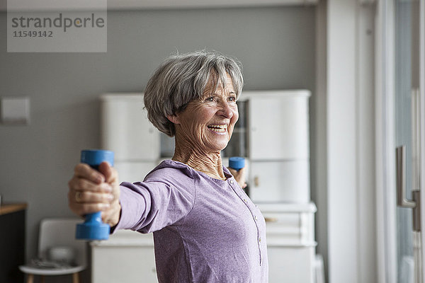Porträt einer glücklichen Seniorin beim Fitnesstraining mit Hanteln zu Hause
