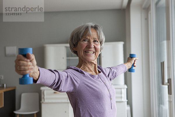 Porträt einer glücklichen Seniorin beim Fitnesstraining mit Hanteln zu Hause