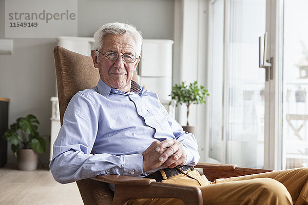 Porträt eines lächelnden älteren Mannes  der zu Hause auf einem Sessel sitzt.