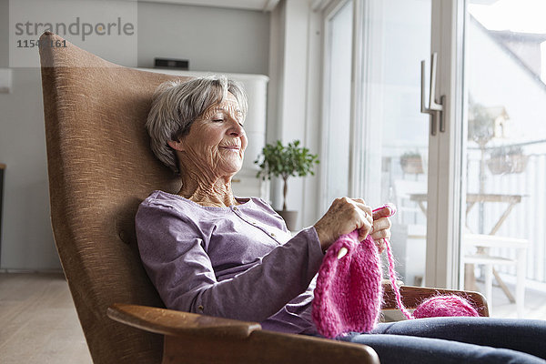 Porträt einer älteren Frau  die zu Hause auf einem Sessel sitzt und strickt.