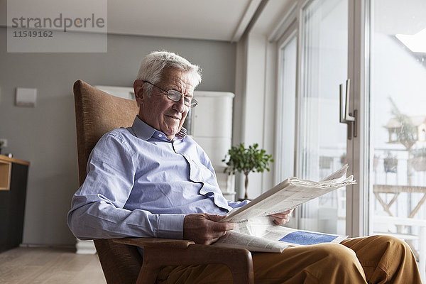 Porträt eines älteren Mannes  der zu Hause auf einem Sessel sitzt und Zeitung liest.
