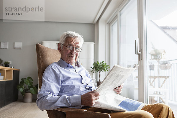 Porträt eines älteren Mannes  der zu Hause auf einem Sessel sitzt und Zeitung liest.