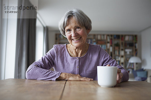 Porträt einer älteren Frau  die bei einer Tasse Kaffee am Tisch sitzt.