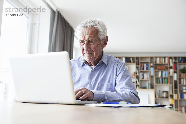 Porträt eines älteren Mannes am Tisch mit Laptop