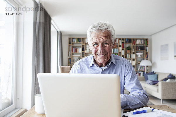 Portrait eines älteren Mannes am Tisch im Wohnzimmer mit Laptop