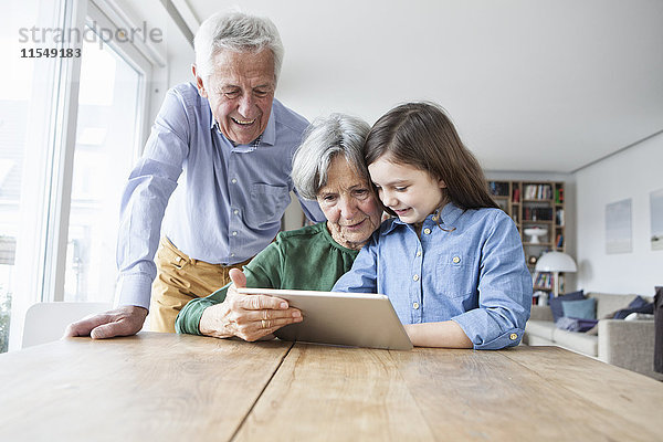 Großeltern und ihre Enkelin beim Betrachten des digitalen Tabletts zu Hause