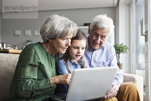 Großeltern und ihre Enkelin sitzen zusammen auf der Couch und schauen auf ein digitales Tablett.