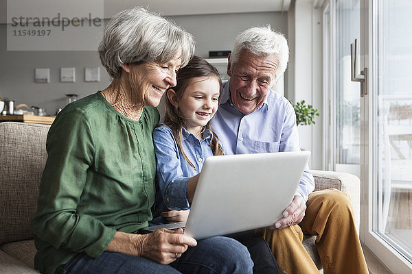 Großeltern und ihre Enkelin sitzen zusammen auf der Couch und schauen auf ein digitales Tablett.