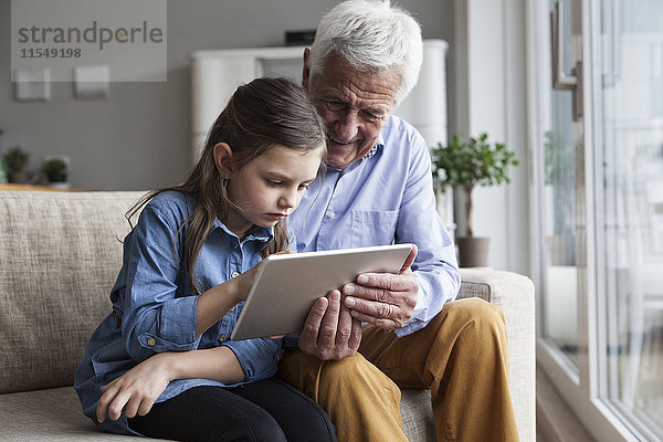 Großvater und seine Enkelin sitzen zusammen auf der Couch mit Hilfe eines digitalen Tabletts.