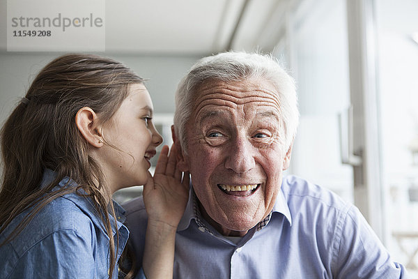 Enkelin  die ihrem Großvater etwas ins Ohr flüstert.