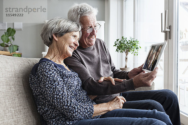 Seniorenpaar sitzt im Wohnzimmer mit digitalem Tablettskyping mit Familie