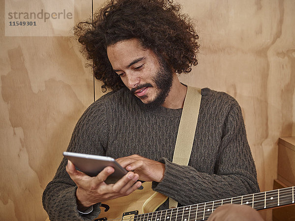 Junger Mann mit E-Gitarre beim Betrachten des digitalen Tabletts