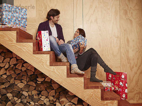 Ein glückliches Paar sitzt auf einer Holztreppe und hält Weihnachtsgeschenke.