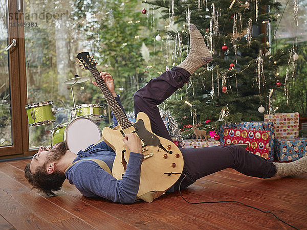 Mann spielt E-Gitarre vor dem Weihnachtsbaum