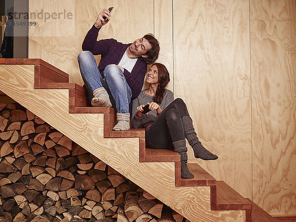 Glückliches Paar sitzt auf einer Holztreppe mit dem Smartphone