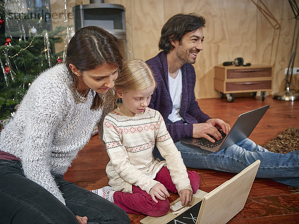 Vater mit Laptop  Mutter spielt mit Tochter auf dem Spielzeugcomputer an Heiligabend