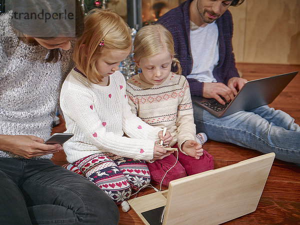 Vater mit Laptop  Mutter spielt am Heiligabend mit Töchtern am Spielzeugcomputer