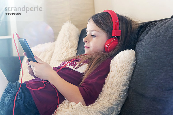 Mädchen sitzt auf der Couch und hört Musik mit Kopfhörer und digitalem Tablett.