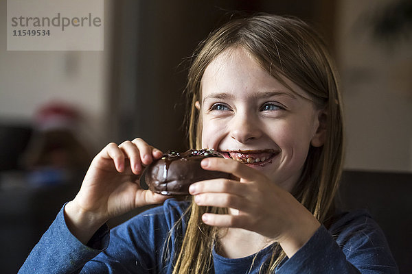 Porträt eines lächelnden Mädchens beim Essen von Schoko-Doughnut