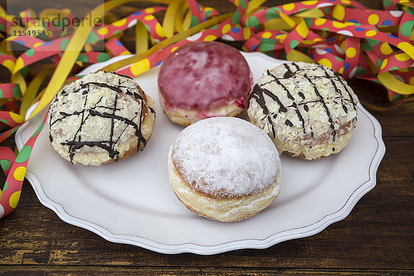 Teller mit vier verschiedenen Marmeladen-Doughnuts und Sieben im Hintergrund