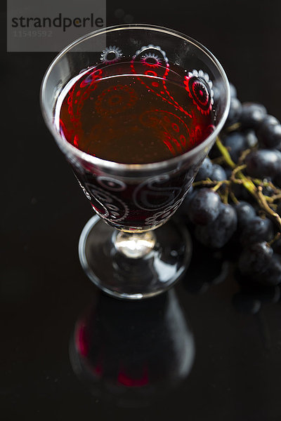 Glas Rotwein und blaue Trauben auf schwarzem Grund