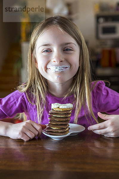 Porträt eines glücklichen Mädchens mit Schlagsahne auf den Lippen und einem Stapel Mini-Pfannkuchen mit Schokolade