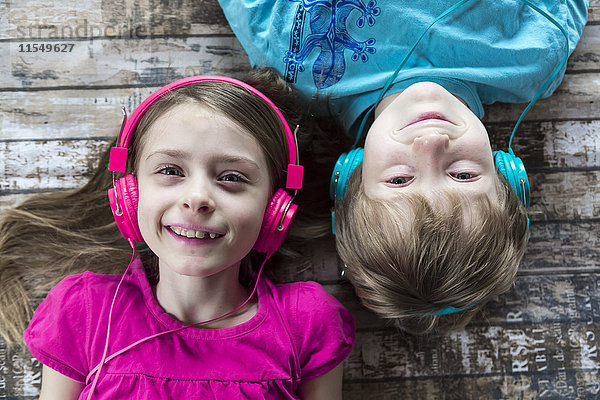 Porträt von Bruder und kleiner Schwester beim Hören von Musik mit Kopfhörern