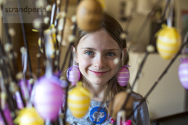 Porträt des lächelnden Mädchens hinter Zweigen von Pussy Weiden mit Ostereiern verziert