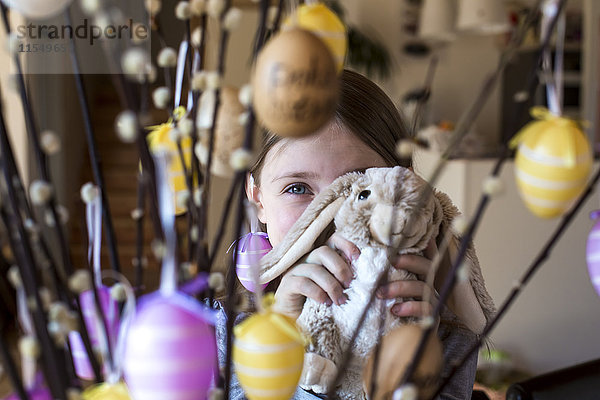 Mädchen versteckt hinter Osterhasen und Weidenzweige mit Ostereiern verziert