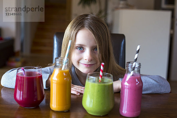 Porträt eines lächelnden Mädchens am Tisch mit vier verschiedenen Smoothies zur Auswahl