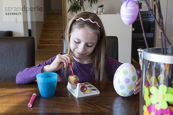 Lächelndes Mädchen malt Osterei zu Hause