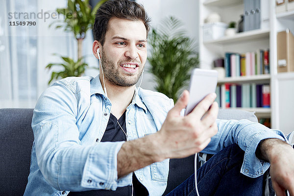 Junger Mann zu Hause mit Smartphone und Ohrhörern