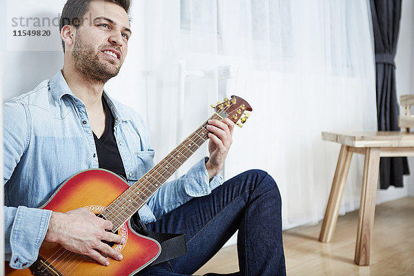 Junger Mann sitzt auf dem Boden und spielt Gitarre.