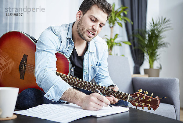 Junger Mann mit Gitarre beim Komponieren eines Liedes
