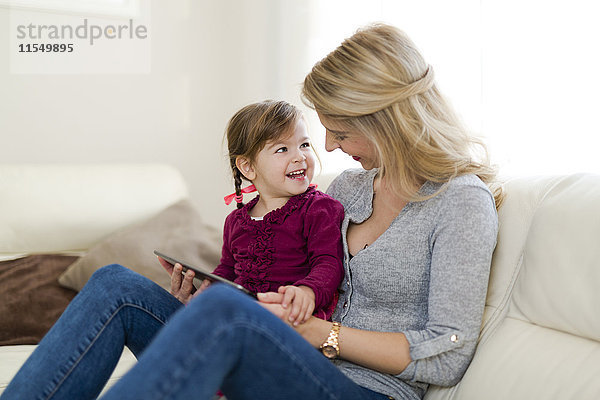Mutter und ihre kleine Tochter sitzen auf der Couch im Wohnzimmer mit digitalem Tablett