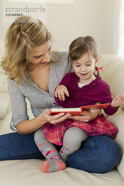 Ein kleines Mädchen sitzt auf dem Schoß seiner Mutter und schaut sich ein Buch an.