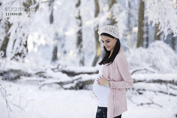 Lächelnde schwangere Frau im Freien bei Schneefall