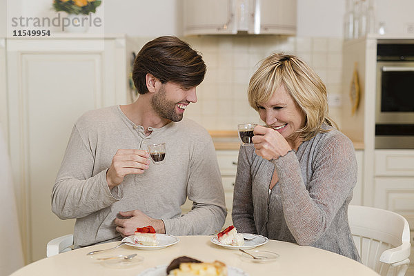 Mutter und erwachsener Sohn trinken Espresso in der Küche und haben Spaß zusammen.