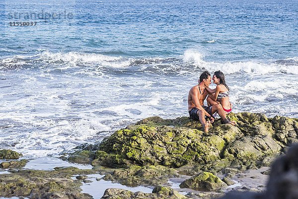 Ein glückliches verliebtes Paar sitzt auf einem Felsen im Meer.