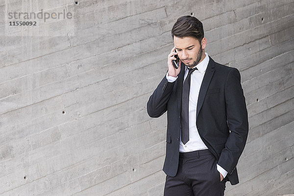 Geschäftsmann im schwarzen Anzug telefoniert mit Smartphone