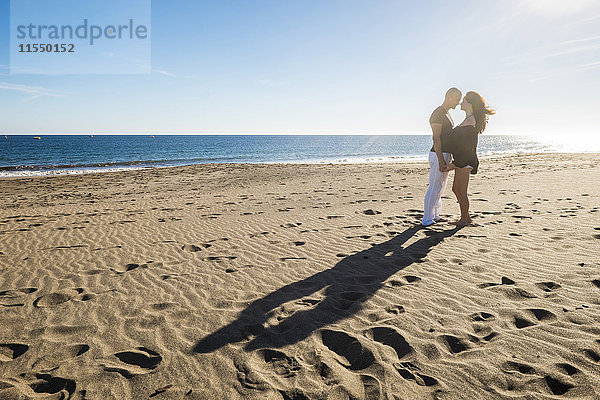 Spanien  Teneriffa  glückliches Paar  das bei Gegenlicht von Angesicht zu Angesicht am Strand steht.