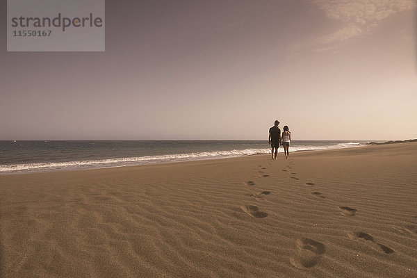 Spanien  Teneriffa  Rückansicht eines verliebten jungen Paares beim Spaziergang am Sandstrand