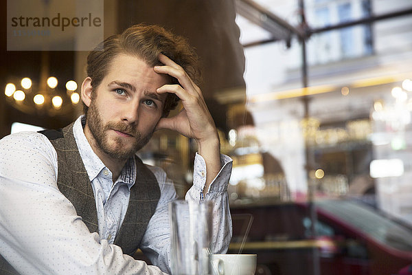 Junger Mann in einem Café mit Blick aus dem Fenster
