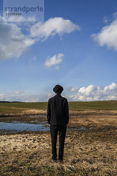 Rückansicht des in schwarz gekleideten jungen Mannes auf der Weide stehend