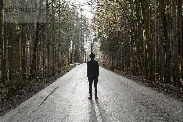 Deutschland  Rückansicht eines schwarz gekleideten jungen Mannes auf leerer Landstraße