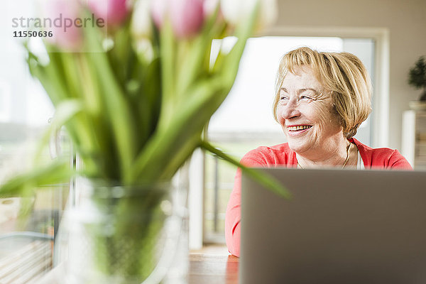 Lächelnde Seniorin am Tisch sitzend mit Laptop