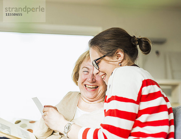 Glückliche Seniorin und junge Frau auf der Couch beim Betrachten des Fotoalbums