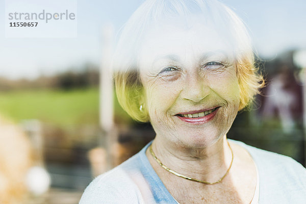 Porträt der lächelnden Seniorin hinter der Fensterscheibe