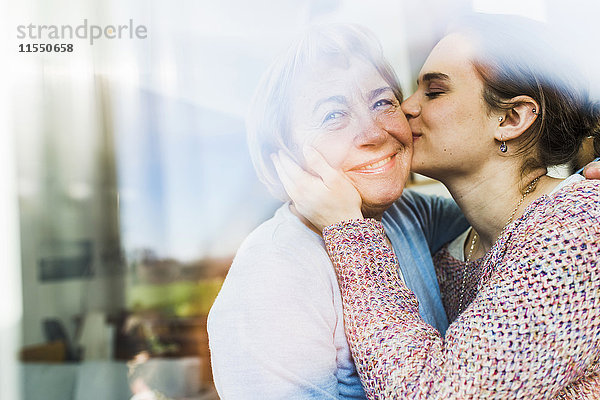 Junge Frau küsst ältere Frau hinter Fensterscheibe